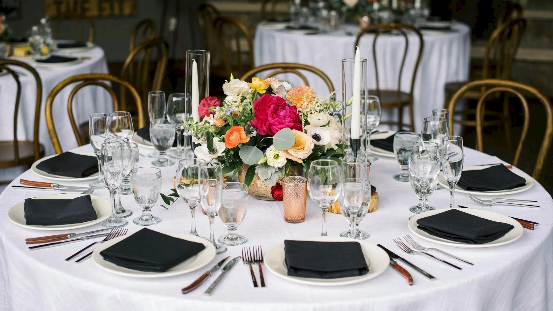 A round table is elegantly set with white tablecloth, black napkins, glassware, cutlery, and a floral centerpiece in a banquet setting ending the sentence.