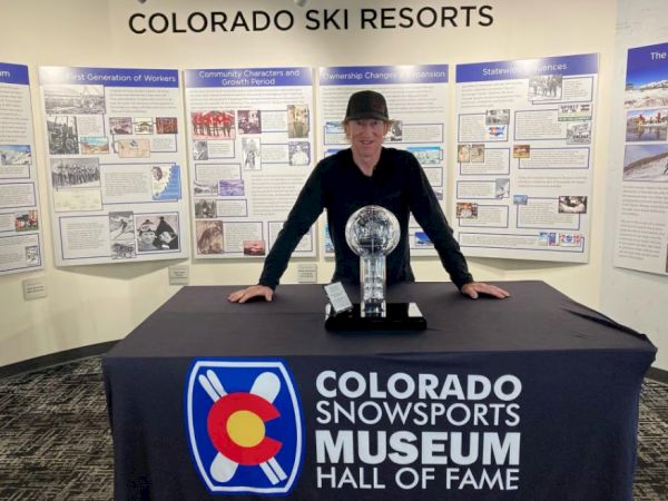 A person stands behind a table with a trophy at the Colorado Snowsports Museum Hall of Fame exhibition.