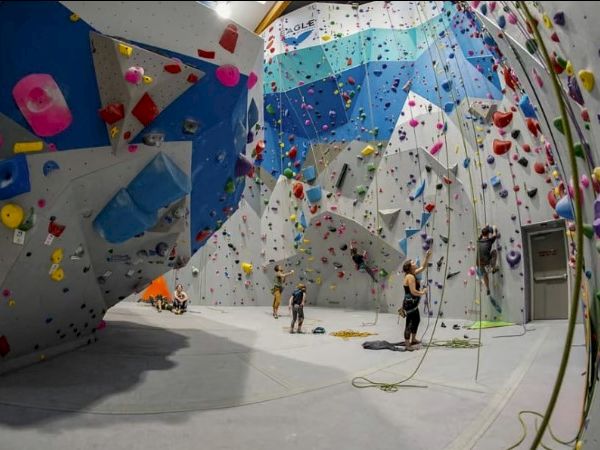 Indoor climbing gym with several people climbing walls, colorful holds, and a variety of climbing routes.